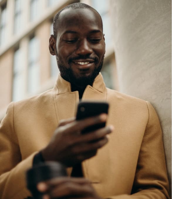 Smiling man in a beige coat looking at his phone, symbolizing connection and engagement.