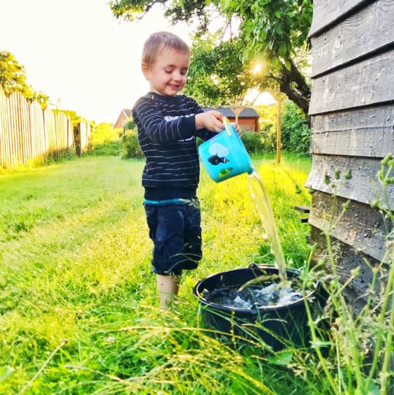 Young boy playing with water outdoors, pouring water into a bucket, representing playful moments in caregiving.